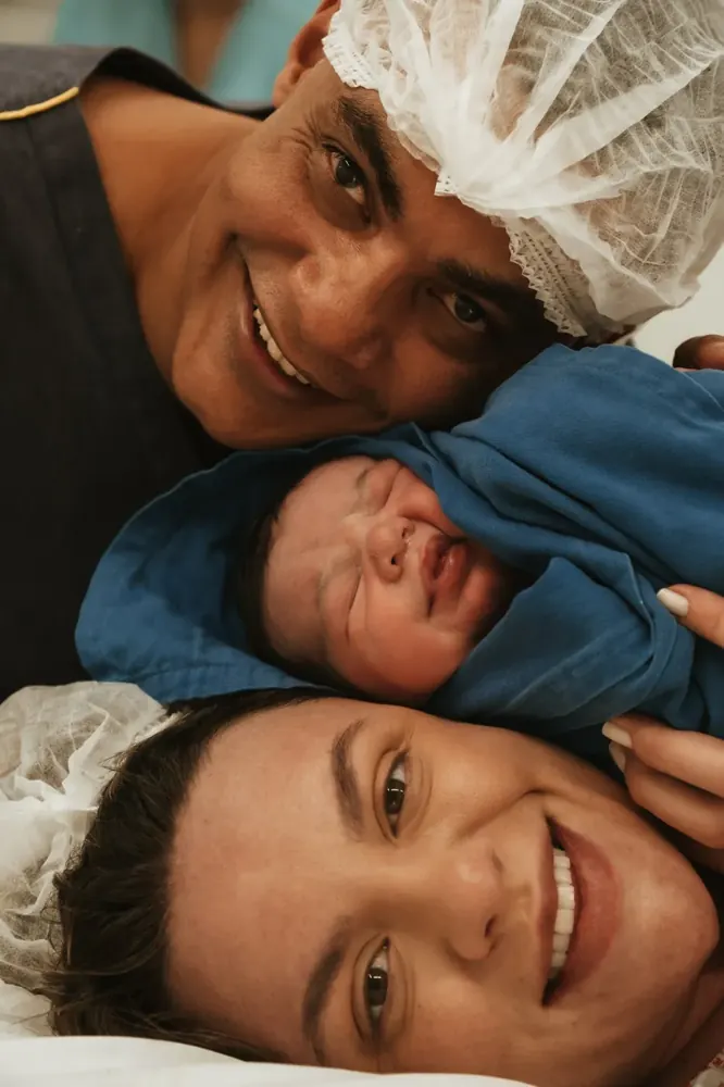 Pais sorriem com o bebê entre eles
